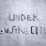 Under construction text creatively formed using various screws and tools on a concrete background.