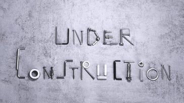 Under construction text creatively formed using various screws and tools on a concrete background.