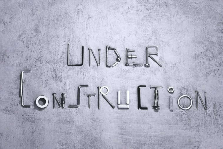 Under construction text creatively formed using various screws and tools on a concrete background.