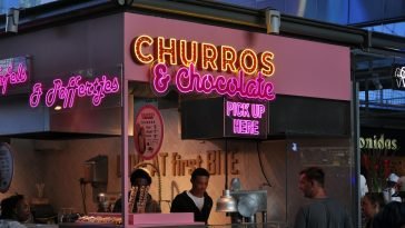 Neon-lit churro and chocolate stand attracting food lovers in an urban market.