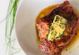 Delicious grilled steak served with a mouthwatering herb butter topping on a white ceramic plate.