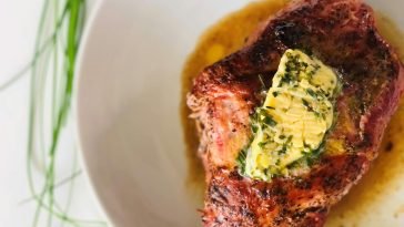 Delicious grilled steak served with a mouthwatering herb butter topping on a white ceramic plate.