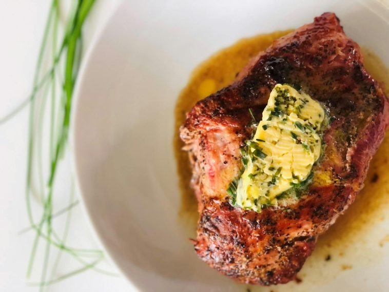Delicious grilled steak served with a mouthwatering herb butter topping on a white ceramic plate.