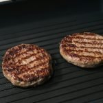 Close-up of juicy grilled beef patties cooking on a flat iron skillet.