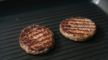 Close-up of juicy grilled beef patties cooking on a flat iron skillet.