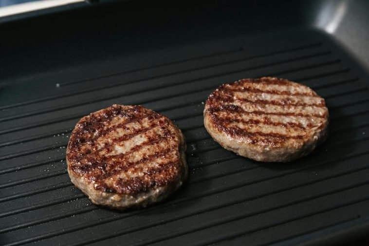 Close-up of juicy grilled beef patties cooking on a flat iron skillet.