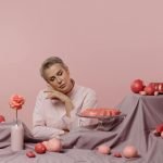 Elegant portrait of a woman surrounded by pink desserts and decor on a pastel background.