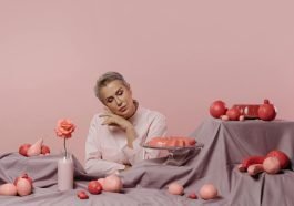 Elegant portrait of a woman surrounded by pink desserts and decor on a pastel background.