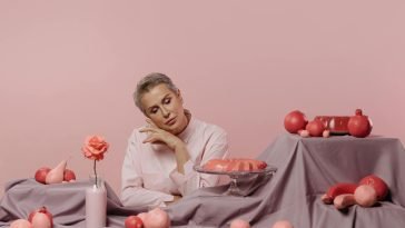 Elegant portrait of a woman surrounded by pink desserts and decor on a pastel background.