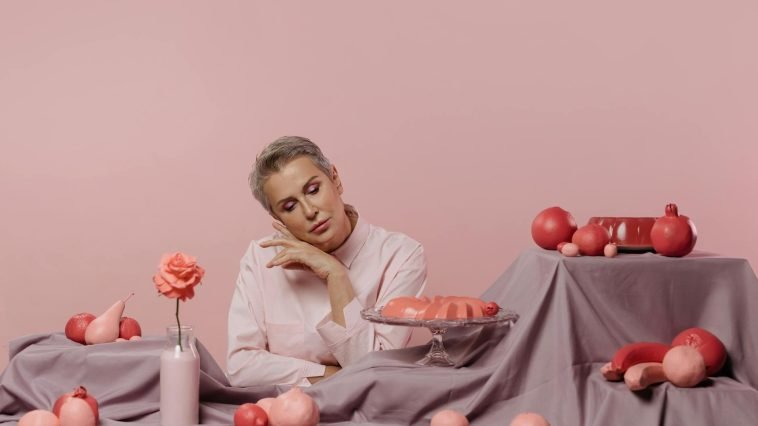 Elegant portrait of a woman surrounded by pink desserts and decor on a pastel background.