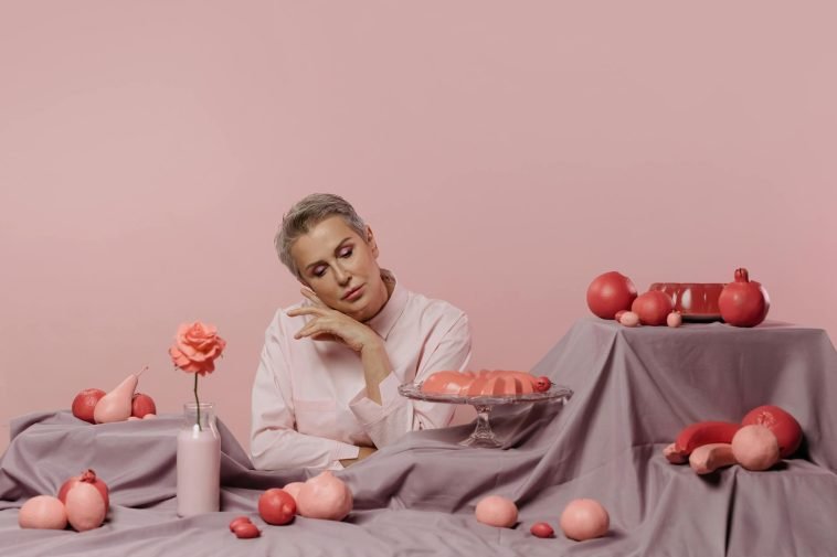 Elegant portrait of a woman surrounded by pink desserts and decor on a pastel background.