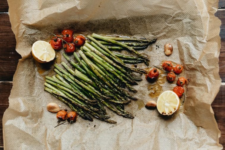 Delicious roasted asparagus with cherry tomatoes and lemon on parchment paper, perfect for a healthy meal.