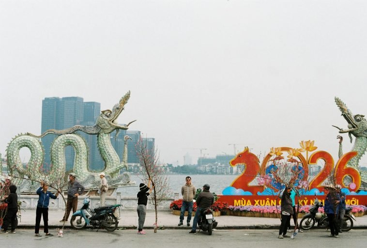 People preparing for Lunar New Year 2026 by a dragon statue along a lakeside.