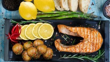Delicious grilled salmon served with lemon slices, potatoes, and asparagus on rustic table.
