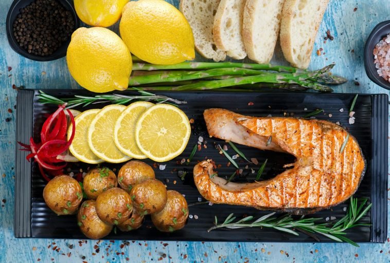 Delicious grilled salmon served with lemon slices, potatoes, and asparagus on rustic table.