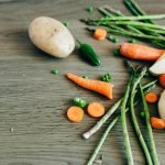 A variety of fresh organic vegetables including carrots, peas, and asparagus on a wooden surface.