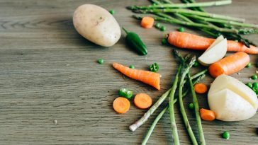 A variety of fresh organic vegetables including carrots, peas, and asparagus on a wooden surface.