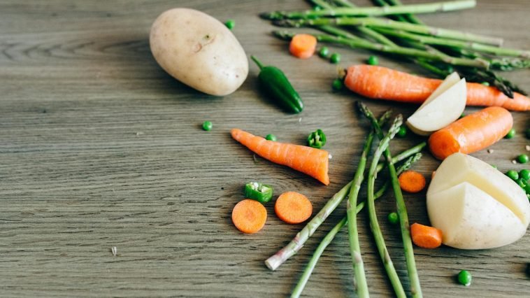 A variety of fresh organic vegetables including carrots, peas, and asparagus on a wooden surface.