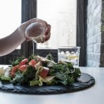 Hand pouring dressing over fresh salad with kale and tomatoes in a modern Dubai restaurant.