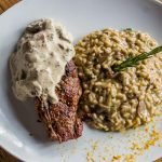 Delicious steak topped with sauce served with creamy mushroom risotto. Italian cuisine on a white plate.
