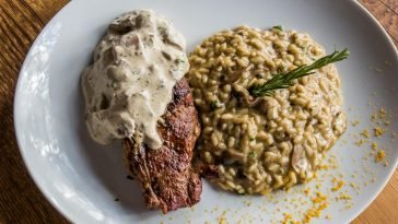 Delicious steak topped with sauce served with creamy mushroom risotto. Italian cuisine on a white plate.