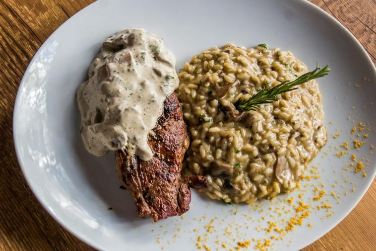 Delicious steak topped with sauce served with creamy mushroom risotto. Italian cuisine on a white plate.