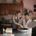Mother and daughter enjoy cooking together in a cozy, rustic kitchen setting.