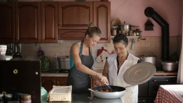 Mother and daughter enjoy cooking together in a cozy, rustic kitchen setting.