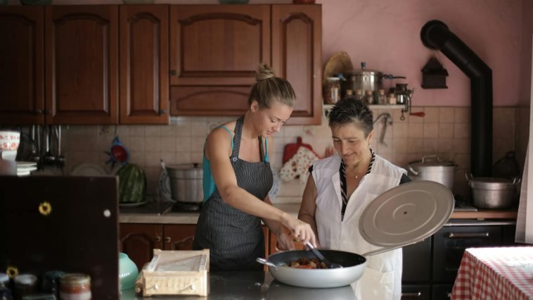 Mother and daughter enjoy cooking together in a cozy, rustic kitchen setting.