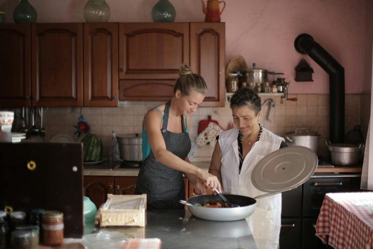Mother and daughter enjoy cooking together in a cozy, rustic kitchen setting.