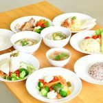 A variety of healthy dishes including rice, soup, and vegetables served on a wooden table.