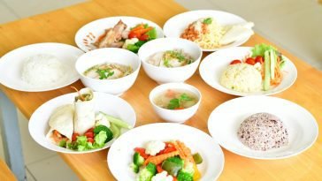 A variety of healthy dishes including rice, soup, and vegetables served on a wooden table.