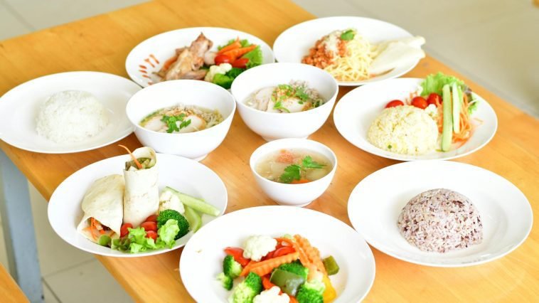 A variety of healthy dishes including rice, soup, and vegetables served on a wooden table.