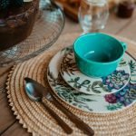 Stylish table setup featuring floral plate, turquoise cup, and woven placemat.