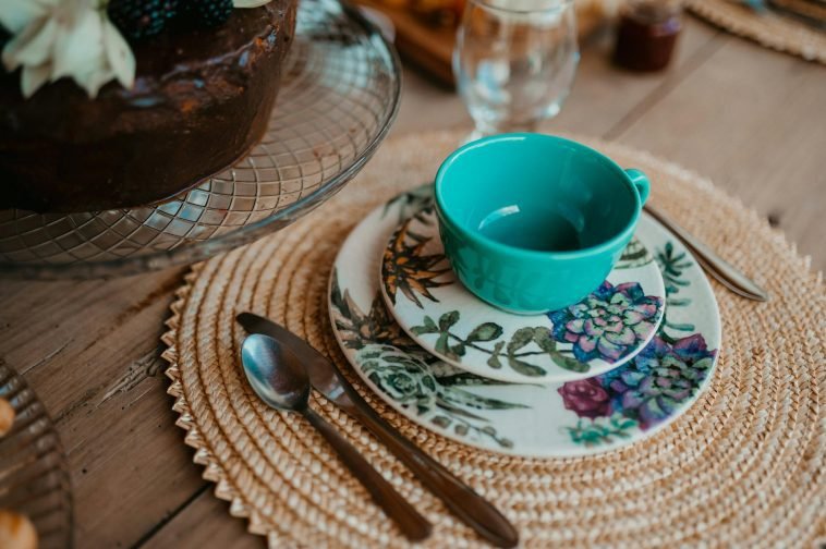 Stylish table setup featuring floral plate, turquoise cup, and woven placemat.