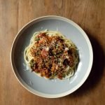 Top view of round plate with delicious Italian pasta Bolognaise garnished with grated parmesan cheese placed on wooden table
