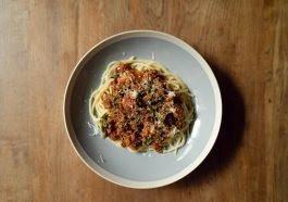 Top view of round plate with delicious Italian pasta Bolognaise garnished with grated parmesan cheese placed on wooden table