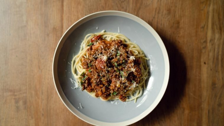 Top view of round plate with delicious Italian pasta Bolognaise garnished with grated parmesan cheese placed on wooden table