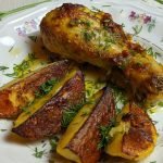 Delicious roasted chicken leg with crispy potatoes garnished with fresh herbs on a floral plate.