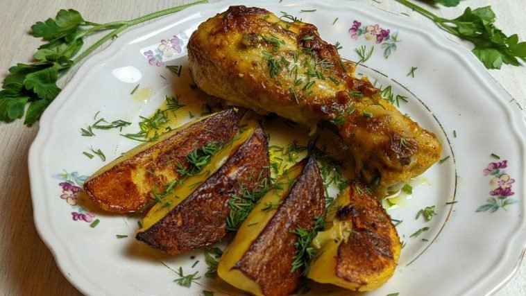Delicious roasted chicken leg with crispy potatoes garnished with fresh herbs on a floral plate.