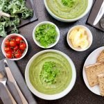 Top view of vegetable soup, bread, and fresh ingredients perfect for a healthy meal.