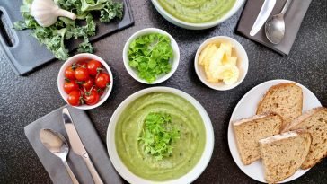Top view of vegetable soup, bread, and fresh ingredients perfect for a healthy meal.