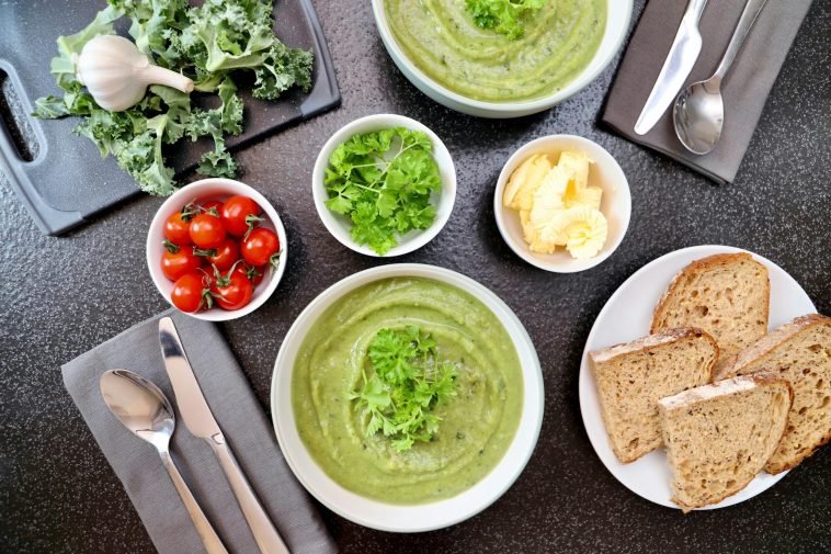 Top view of vegetable soup, bread, and fresh ingredients perfect for a healthy meal.