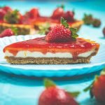 A tempting slice of strawberry cheesecake garnished with fresh strawberries on a blue plate.