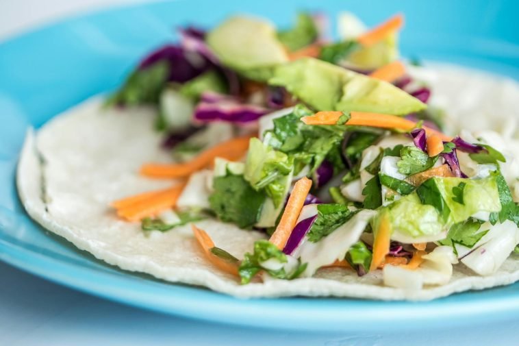 Close-up of a vibrant taco with fresh vegetables on a blue plate.