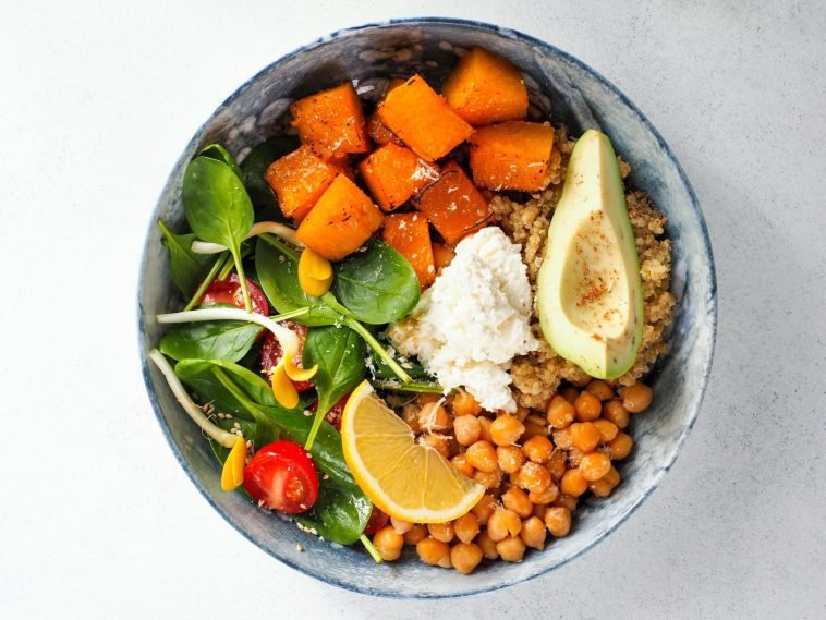 Top view of a colorful vegan buddha bowl featuring avocado, chickpeas, sweet potato, spinach, lemon, and quinoa.