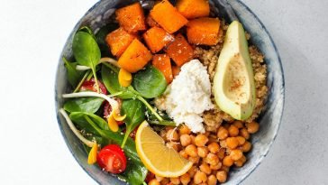 Top view of a colorful vegan buddha bowl featuring avocado, chickpeas, sweet potato, spinach, lemon, and quinoa.