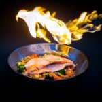 Vibrant flame-grilled salmon served on vegetable fried rice, set against a striking black background.