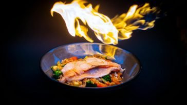 Vibrant flame-grilled salmon served on vegetable fried rice, set against a striking black background.