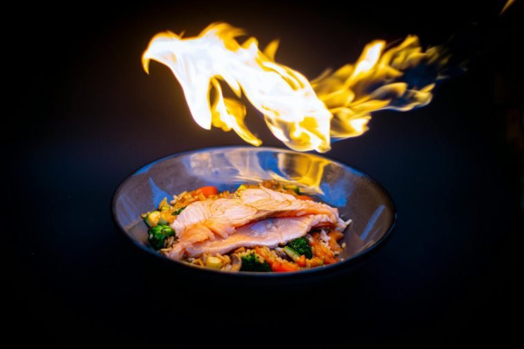 Vibrant flame-grilled salmon served on vegetable fried rice, set against a striking black background.